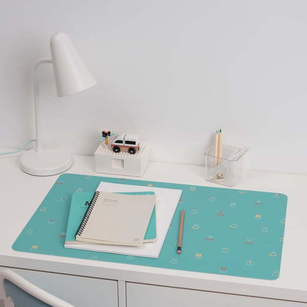 Turquoise BÖNSYRSA desk pad with colourful pattern. Fits well with notebooks and pencil, near lamp and toy truck.