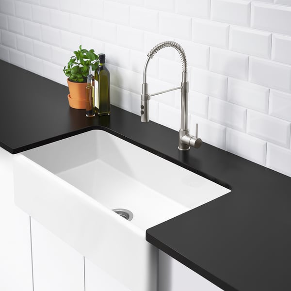 Modern sink with curved tap, plant, bottles on dark counter.
