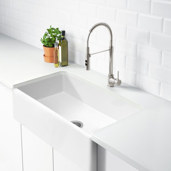 White farmhouse sink, stainless tap, plant, oil bottles, white tiles.