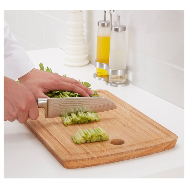 A person chops vegetables on a bamboo cutting board with a stainless steel knife, showcasing the knifes sharpness and durability.