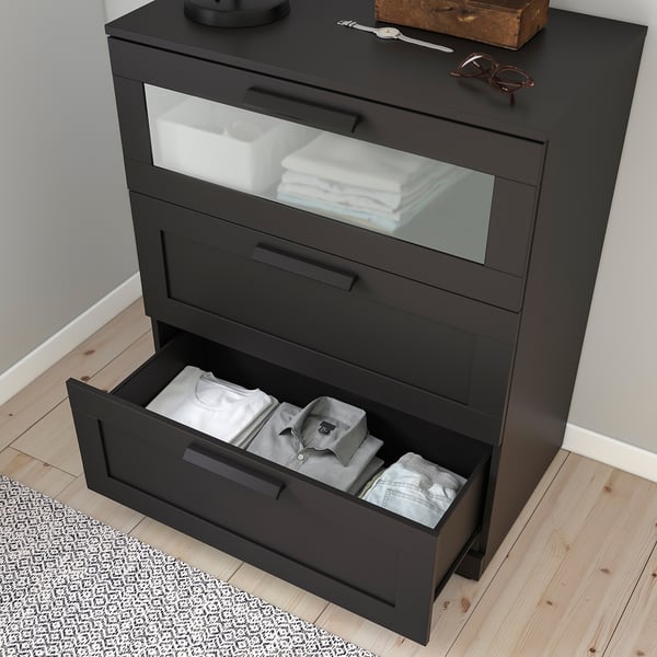 Black chest of drawers with frosted glass top drawer open, showing neatly folded clothes. Drawers extend smoothly.