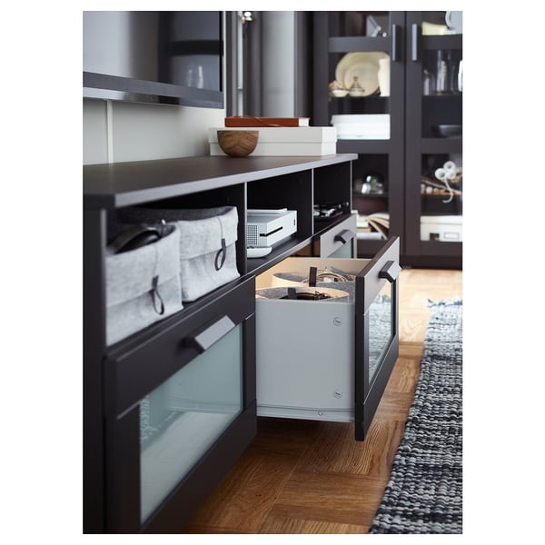 Modern black tv stand with glass doors. Hides cables, contains accessories like remotes.