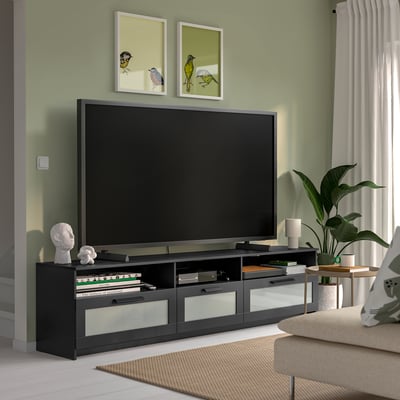 Large black BRIMNES tv stand with glass drawers holds a big flat screen tv, surrounded by living room decor.