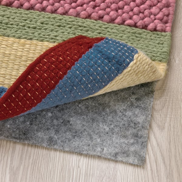 Bright, multicoloured woven rug with varying textures, laid over a grey non-slip pad on wooden floor, showcasing its handcrafted quality.