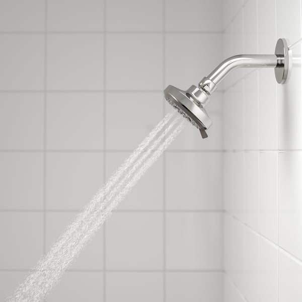 Silver showerhead with wide spray, mounted on white tiles. Water streams out, demonstrating its functional spray.