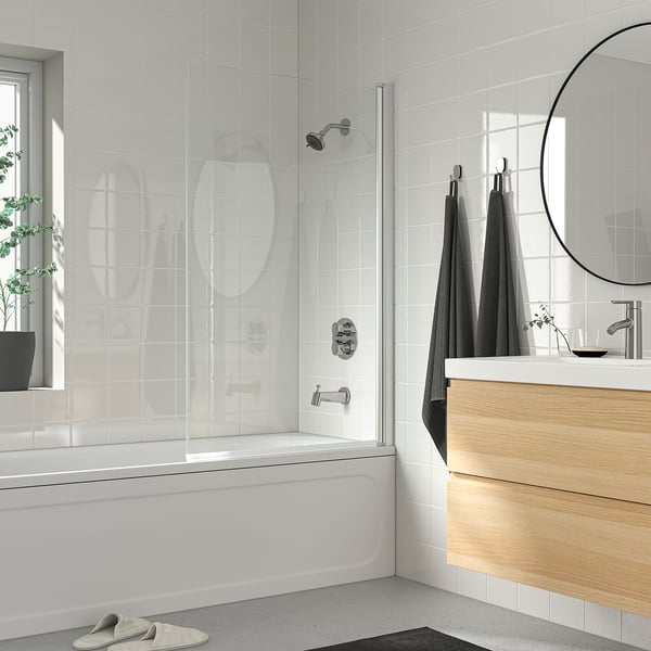 Modern bathroom with tiled walls, wooden vanity, and large chrome BROGRUND showerhead. Glass shower door adds elegance to minimalist design.
