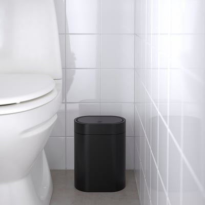 Black rubbish can in bathroom next to white toilet, designed to fit in small spaces.