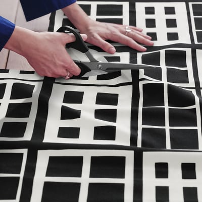 A person cuts pre-cut fabric with black and white windowpane pattern for sewing projects.