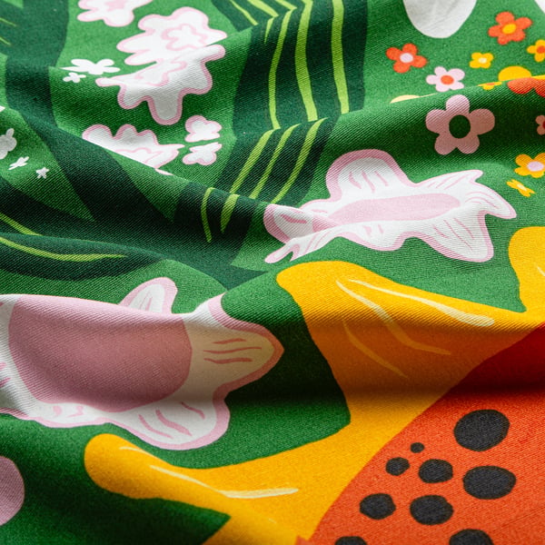 Bright, colourful fabric with large sunflowers and leaves on green, draped elegantly, displaying quality cotton texture.
