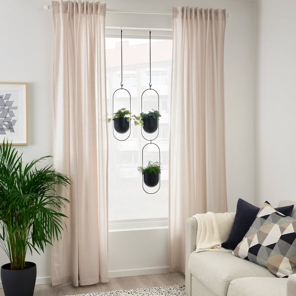 Modern living room with hanging plants, beige curtains, grey sofa, and tall plant.