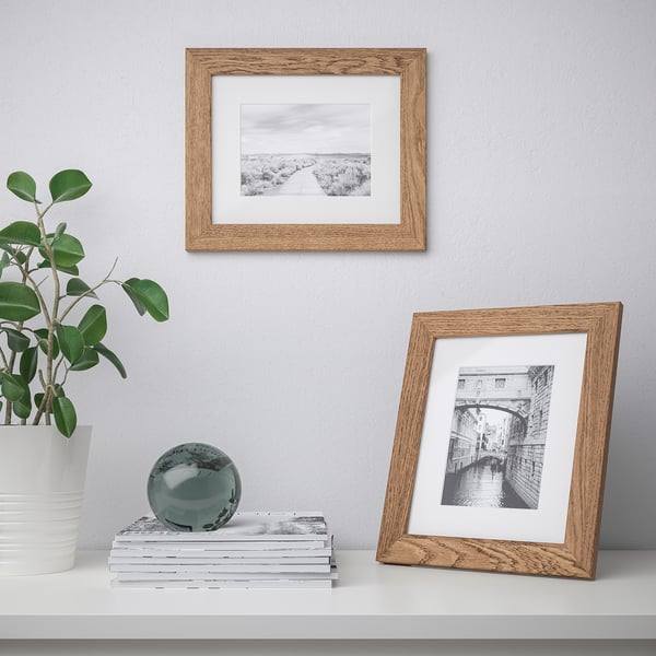 Two wooden photo frames, one mounted, one standing, on a shelf with plants and decor.