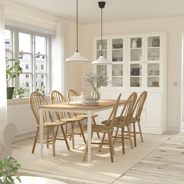 Modern dining set with 6 acacia chairs around a wooden table, vase centrepiece in a minimalist room with natural light.