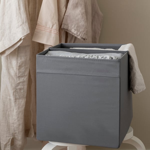 A grey organiser box with a removable divider, placed on a stand, used to separate neatly folded clothes.
