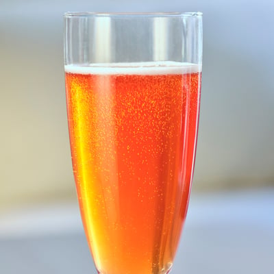 Clear glass cup filled with bubbly, orange-yellow juice, likely apple and lingonberry flavoured, standing upright.