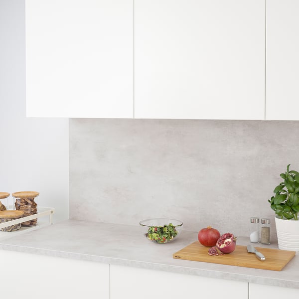 Modern kitchen counter with white cabinets, a glass bowl of salad, pomegranates, a cutting board and knife, potted plant, and wooden storage.