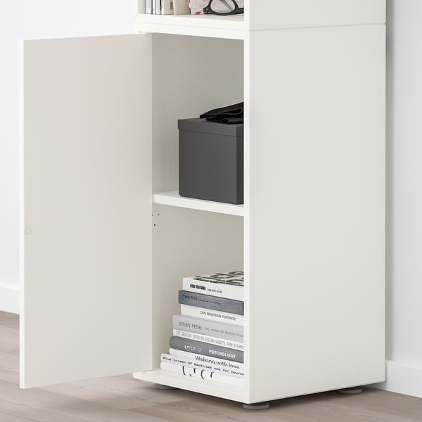 White EKET shelving unit with adjustable shelves, displaying books and a box. A door with a push-opener hides additional storage.