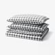 A stack of black and white gingham chequered bedding set including a duvet cover and two pillowcases, made of 100% organic cotton.