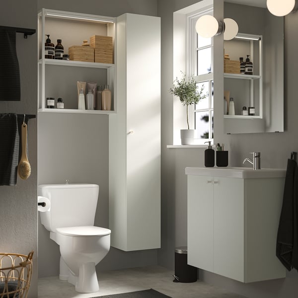 Modern white bathroom with ENHET series: tall cabinet, sink, toilet; open shelves, towels, plant.
