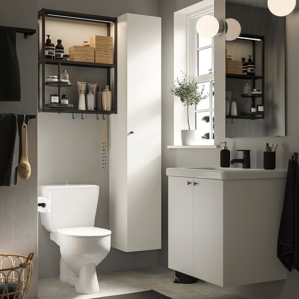 Modern bathroom with white ENHET storage unit, toilet, sink, and mirror. Shelves hold toiletries and plants.