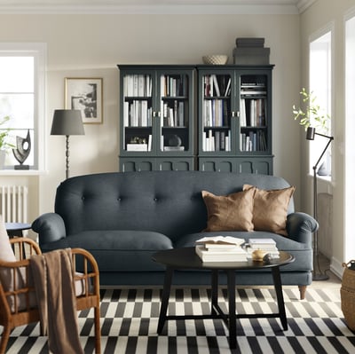 Modern living room with ESSEBODA dark blue sofa, plaid rug, black bookshelf, wooden chair, and floor lamp.