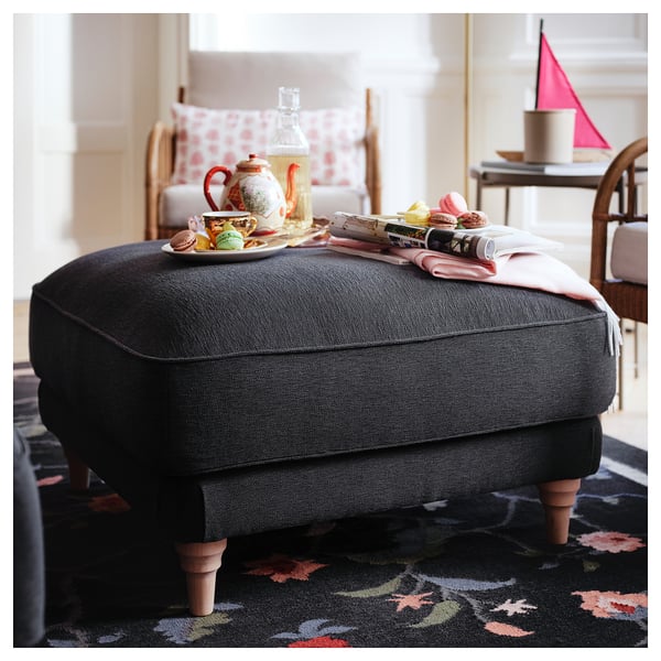 Cosy grey upholstered footstool with wooden legs, displaying tea set and pastries.
