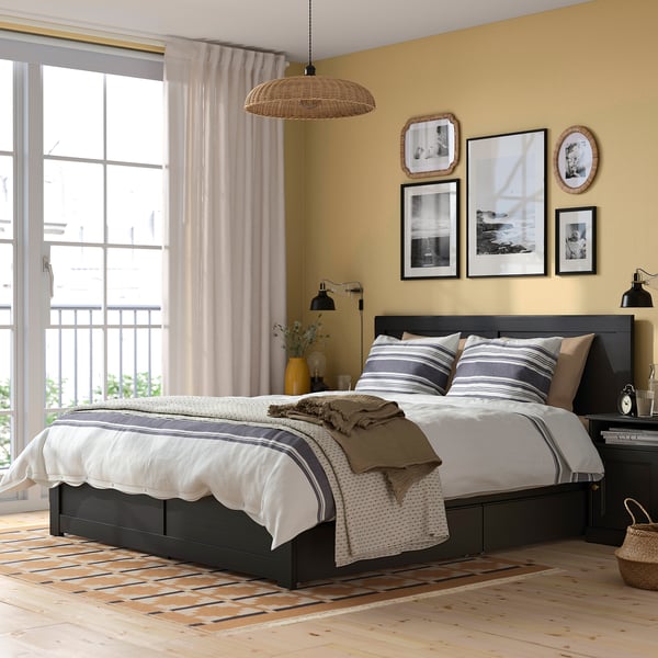 Cosy bedroom with black bed, yellow walls, balcony, and bedside table.