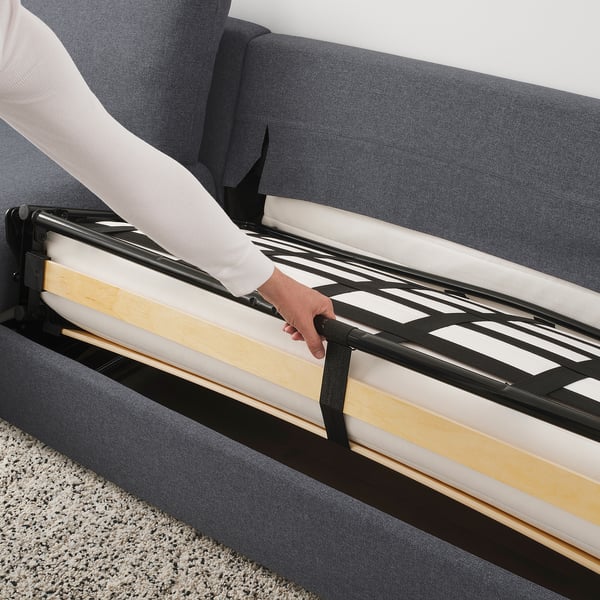 Person pulling out sofa-bed frame from FINNALA sofa, revealing slats and mattress cover.