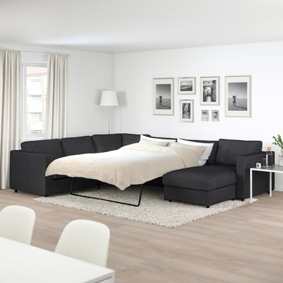 Modern living room with large FINNALA grey sofa-bed, white decor, black frames, and natural lighting.