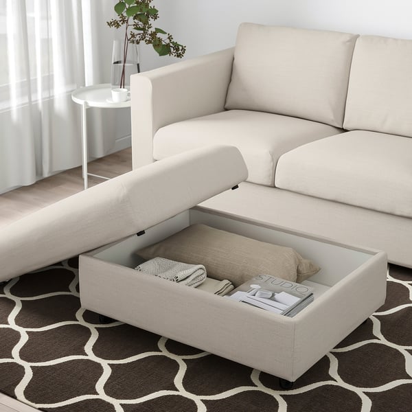 Beige FINNALA sofa with storage ottoman, holding blankets and magazines.