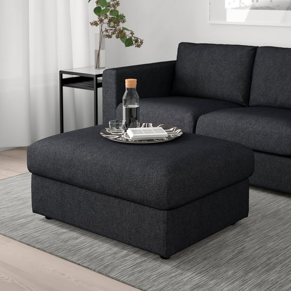 Dark grey footstool with chenille cover & storage, beside sofa with tray, minimalist decor.
