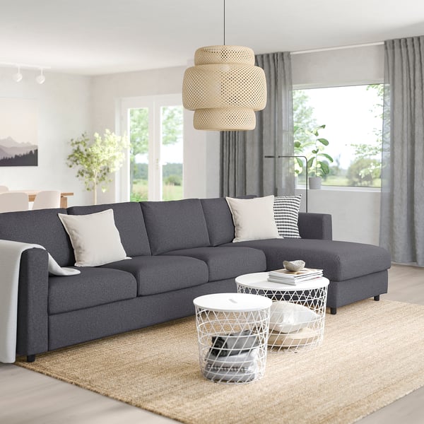 Grey sectional sofa with white cushions, wire tables, jute rug, natural light, pendant light, window with curtains.