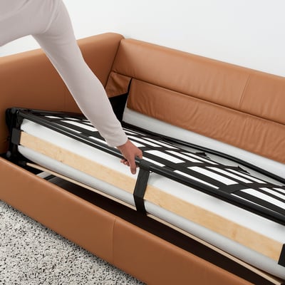 Person transforming FINNALA sofa-bed, revealing thick mattress and sturdy frame.
