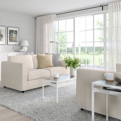 Modern living room with FINNALA sofa, coffee table, lamp, and plants. Large windows and art on walls.