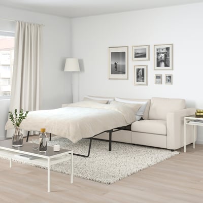 FINNALA sofa-bed in beige, minimalist design, fits well in spacious room, includes multiple decor items.