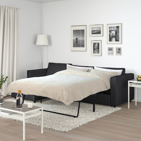 Modern bedroom with FINNALA black sofa-bed, white pillows, black & white photos, white lamp, side tables. Spacious and minimalist.