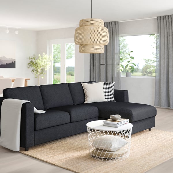 Modern living room with FINNALA grey sectional, black & white pillows, white side table, natural rug, hanging light, plant, and large window.