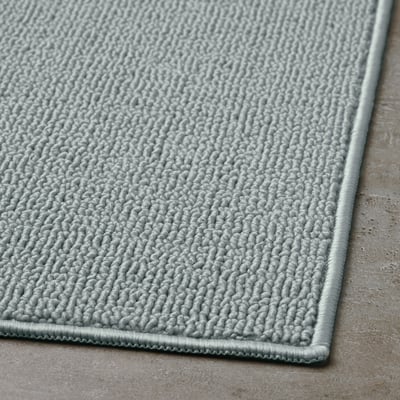 Light grey bath mat with a textured, looped fabric surface and a smooth border, displayed on a flat surface.