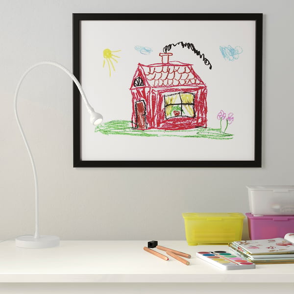 Kids artwork in FISKBO frame on wall. Drawing of red house, green lawn, butterflies. Desk with art supplies, lamp.