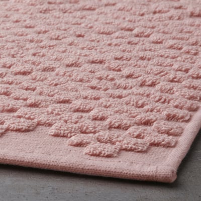 Close-up of a soft, textured, pale pink bathroom mat with raised patterns, showcasing its high-quality, absorbent cotton material.