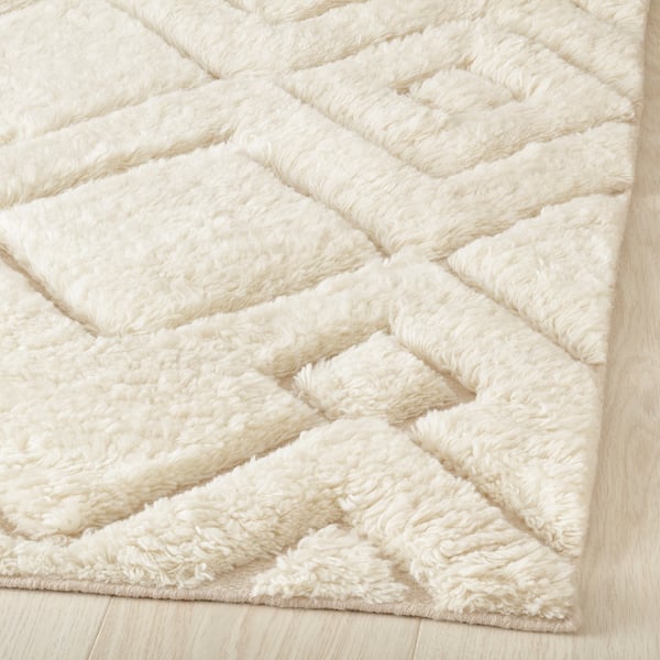 Soft, cream-colored rug with geometric patterns. High and low pile textures create depth. Handwoven, cosy, perfect for living spaces.
