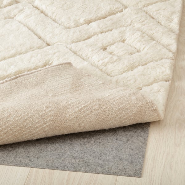 Plush cream rug with geometric design, corner lifted to show grey underlay for comfort and grip.