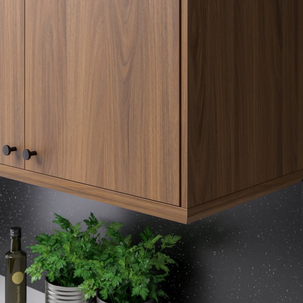 Wooden kitchen cabinet with dark knobs and grey backsplash. Herbs and bottle on counter.
