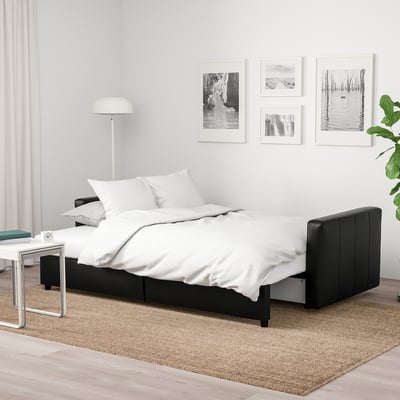 Modern minimalist bedroom with FRIHETEN sleeper sofa, nature prints, floor lamp, and jute rug.