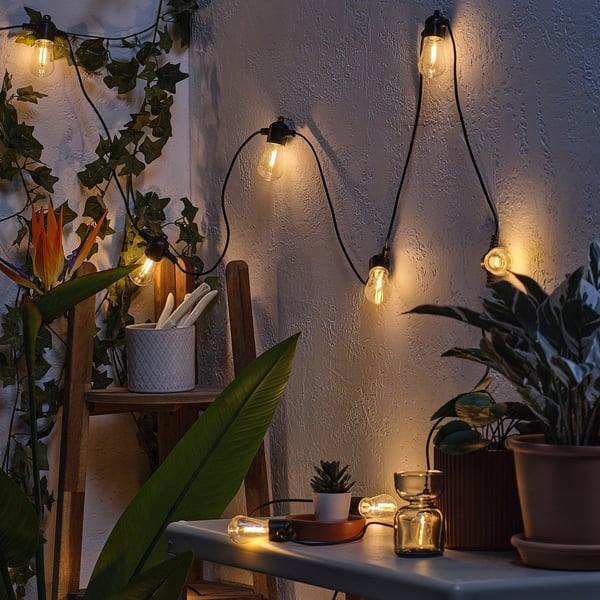 Cosy balcony lighting: string lights illuminate a evening setting with potted plants and wooden furniture, creating a warm outdoor atmosphere.