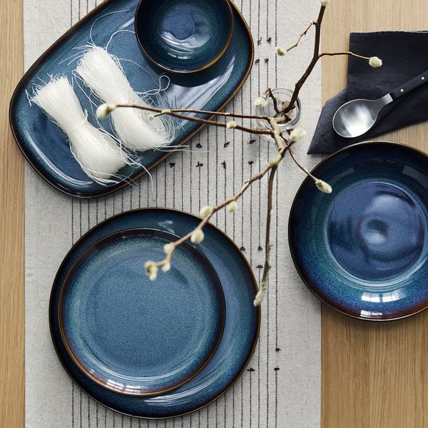 Ocean-blue GLADELIG glazed bowls with golden trim on striped table runner, smaller than plates, adorned with white flowers.