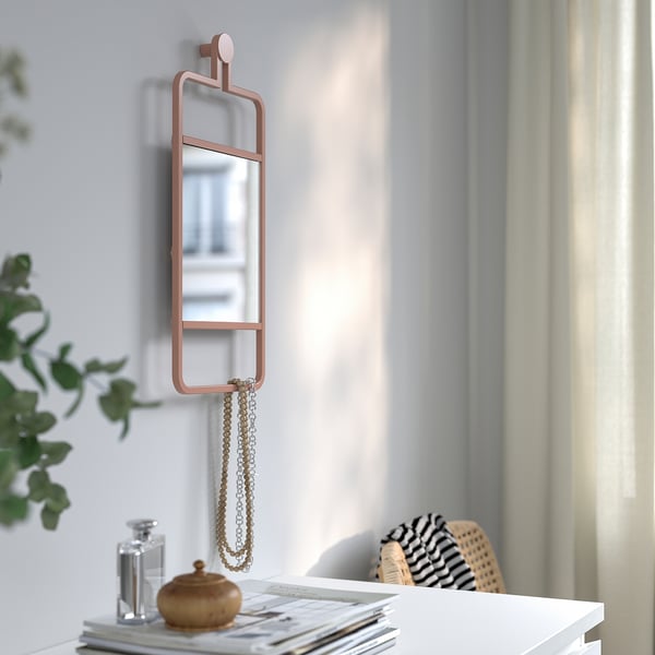 Decorative mirror with copper frame holds necklace, reflecting a window view.
