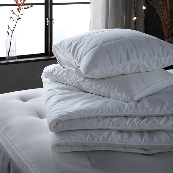 Folded white GRÖNAMARANT pillows on bed, pure cotton, supportive core, fluffy outer filling.