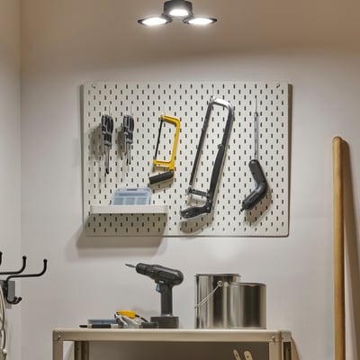 Wall-mounted pegboard holds various tools and equipment. Led light overhead illuminates the workspace.