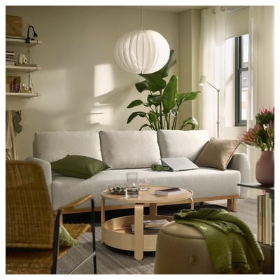 Warm living room: beige sofa-bed, wooden coffee table with glass, large plant, hanging white lamp, tower shelf, cosy decor, natural light.