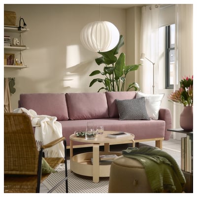 A cosy living room with a light purple GRUNNARP sofa-bed, round light wood coffee table, and a large plant, illuminated by a white pendant lamp.